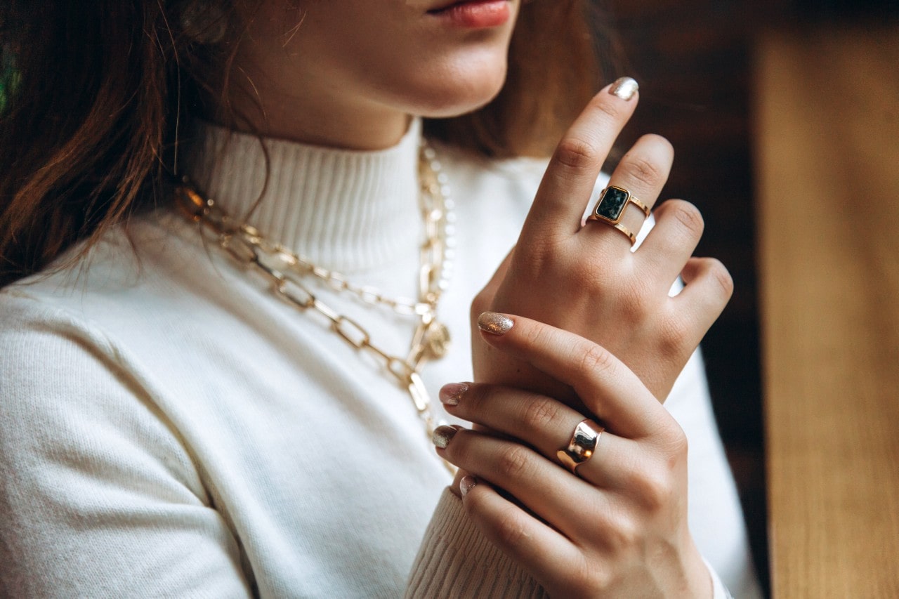 a woman looking out a window and wearing bold yellow gold jewelry