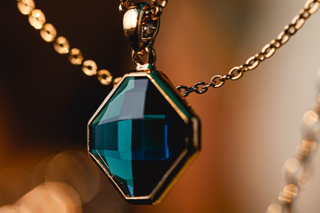 close up image of a yellow gold pendant necklace with a dark teal gemstone