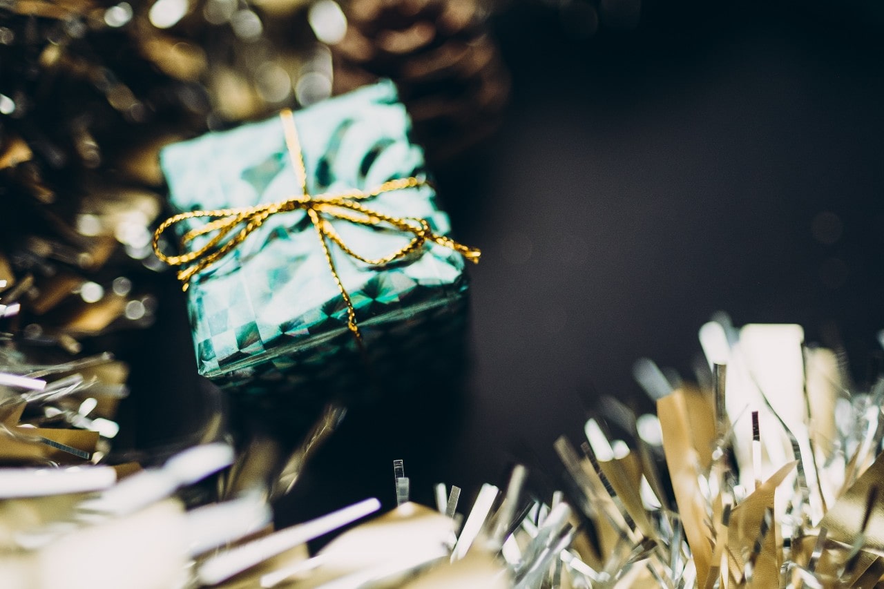 A small gift wrapped in green paper and gold twine surrounded by gold tinsel