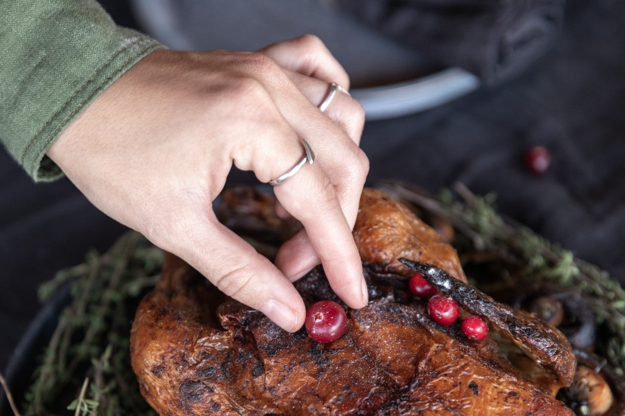 A hand arranging cranberries on a cooked chicken