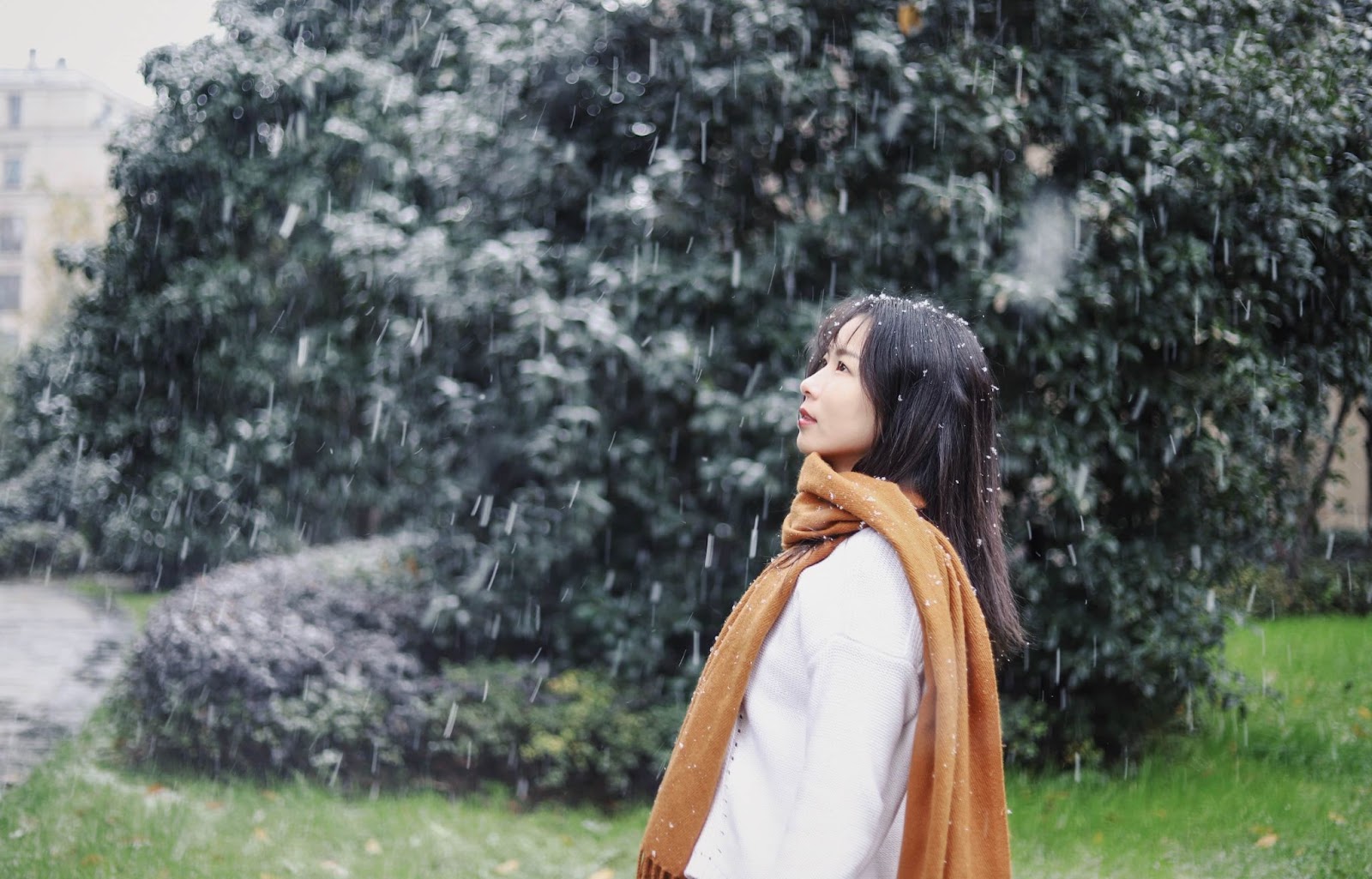 A woman standing in the snow, looking up, wearing a brown scarf