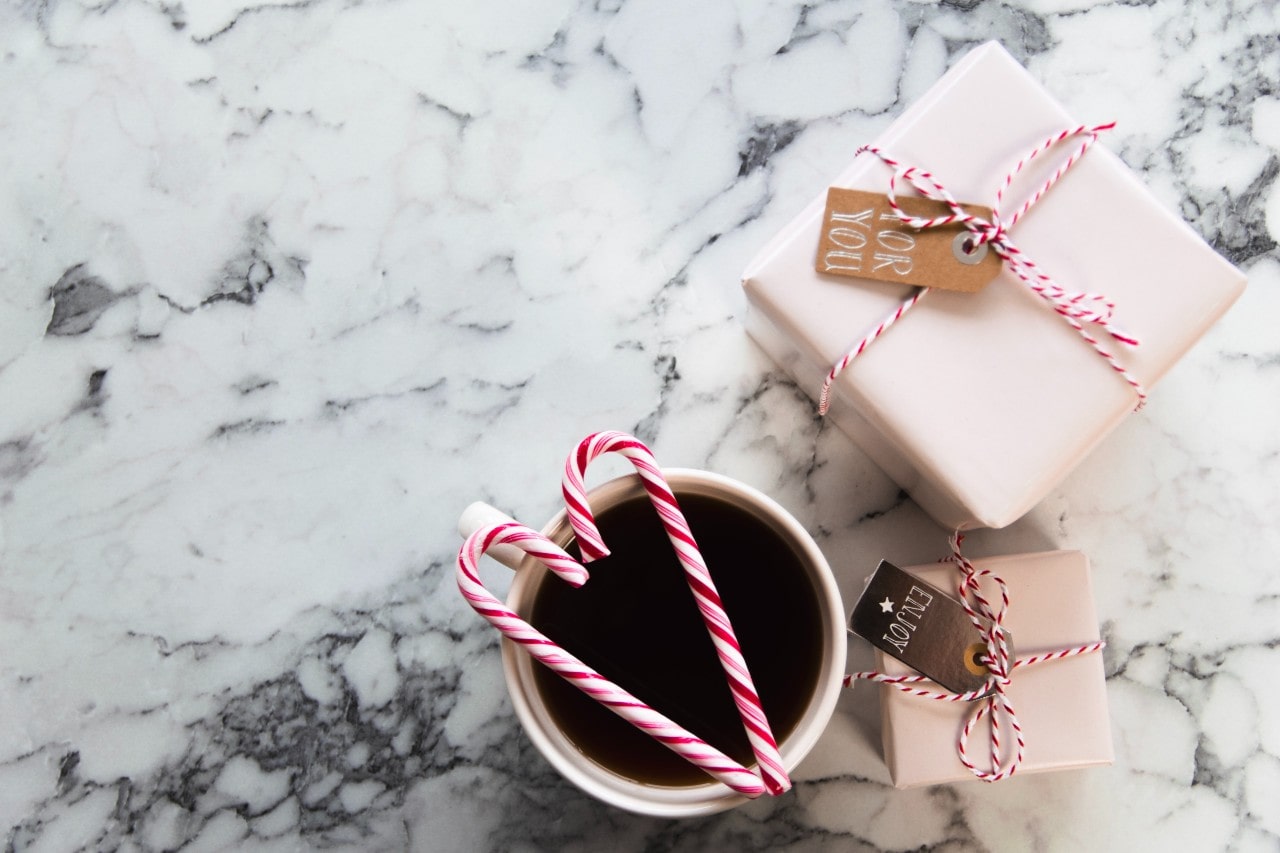 Two candy canes arranged in a heart over a cup of coffee next to two wrapped gifts