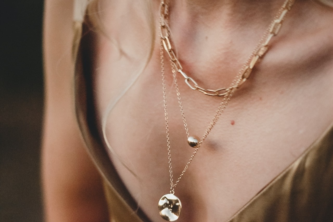 A woman wearing a paperclip yellow gold chain, a metal pendant, and a large gemstone necklace
