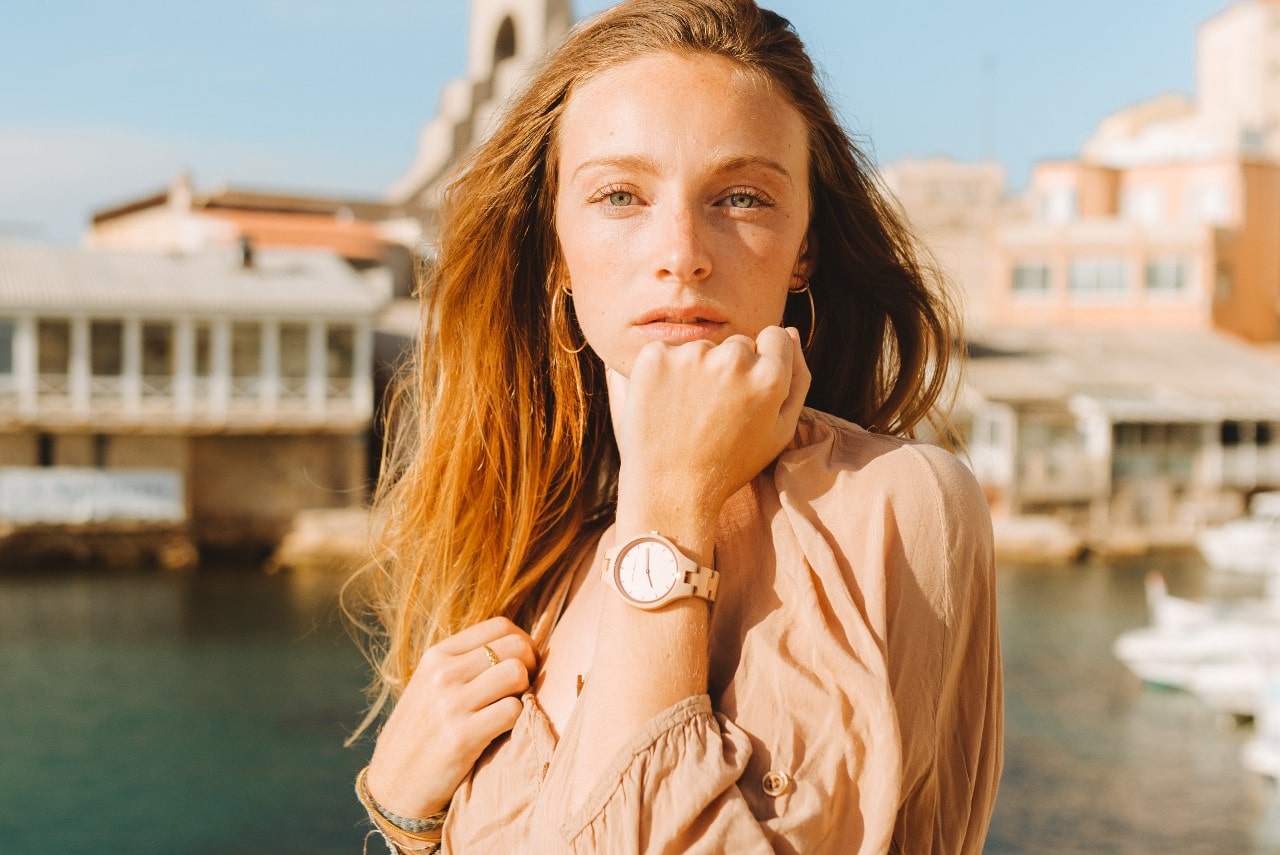 A woman on a canal wearing a rose gold watch, hoop earrings, and bracelets