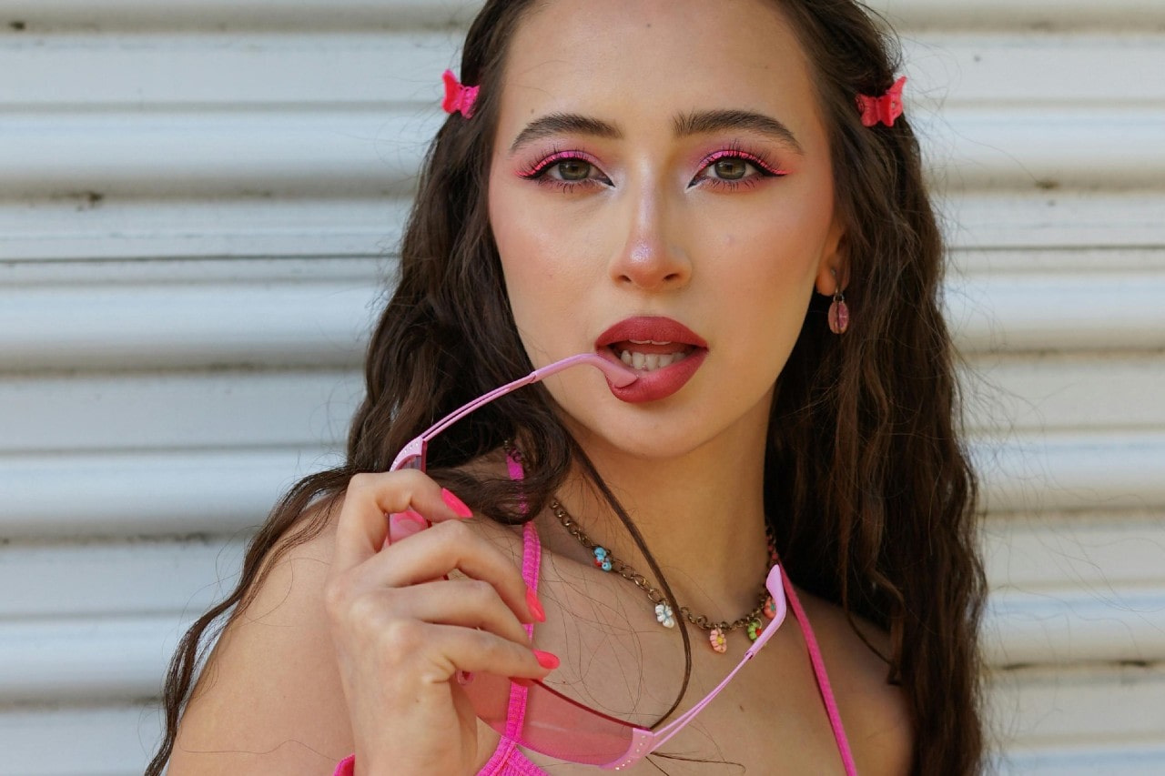 a lady wearing colorful jewelry and holding a pair of pink sunglasses