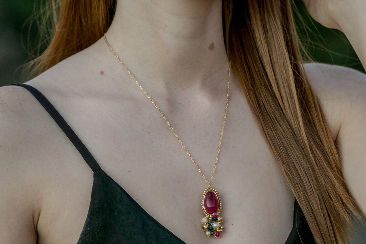 A woman wearing a black tank top sports a colorful gemstone pendant.