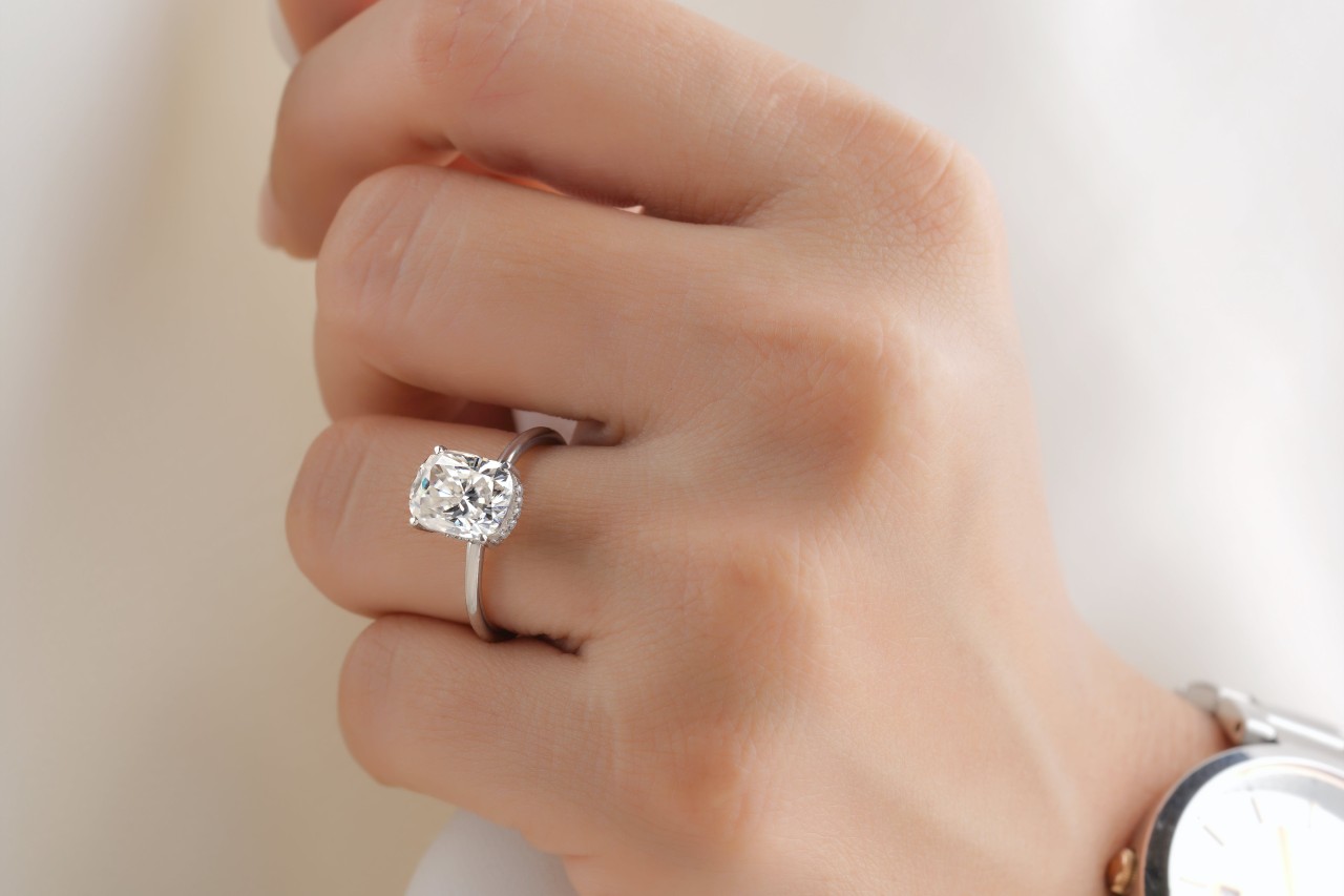 A closeup of a woman’s hand with a platinum solitaire engagement ring.