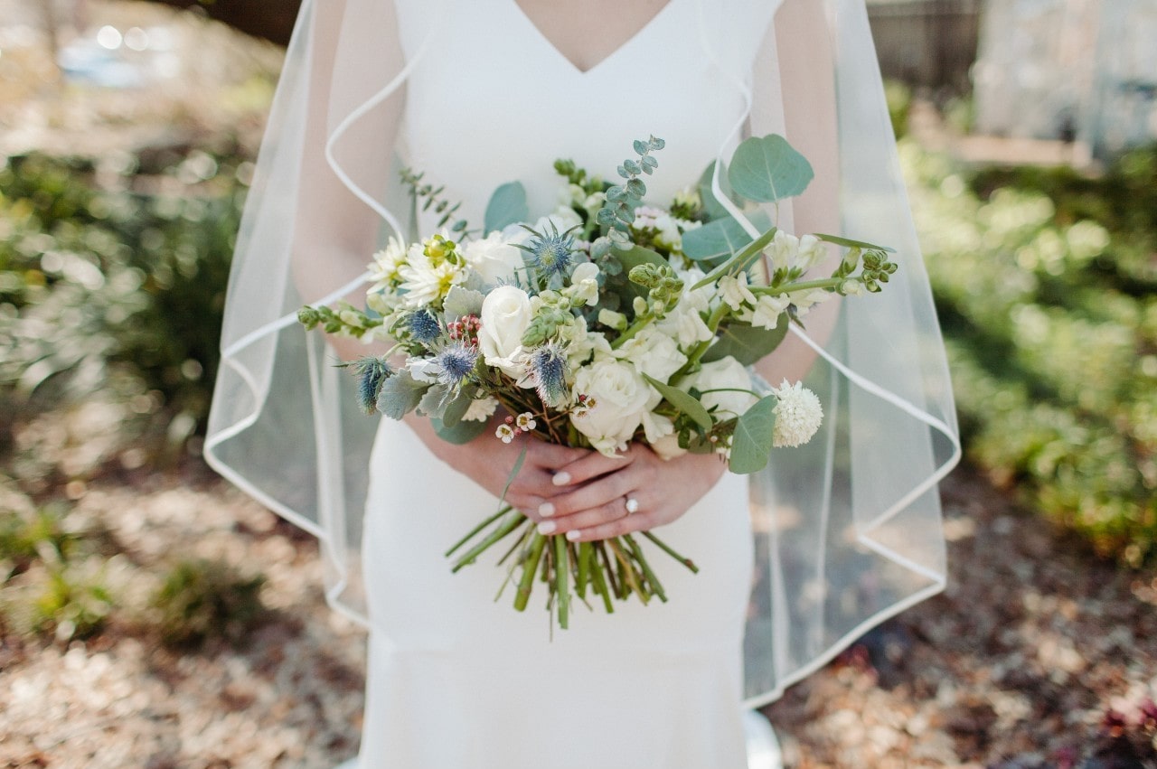 A bride holds her bouquet outside with a veil over her head.