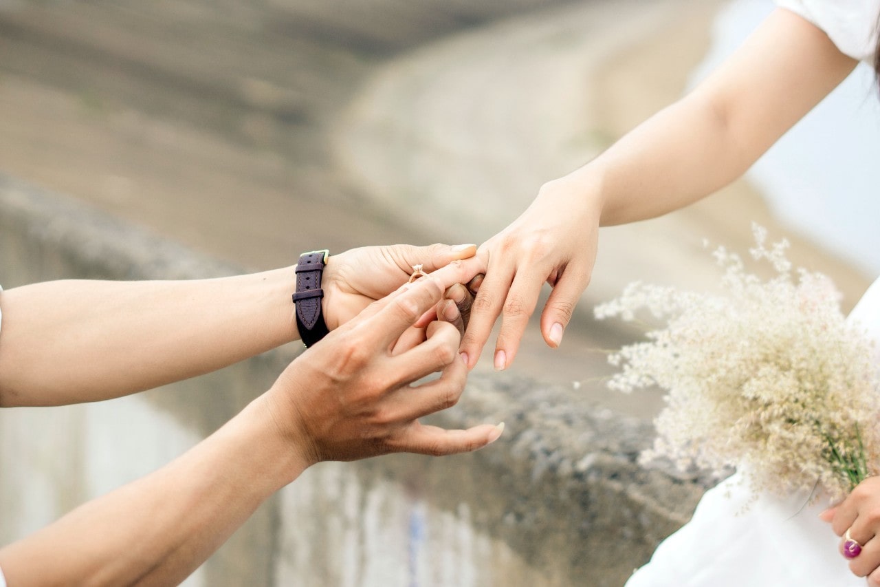 A man slips a simple engagement ring on a woman’s finger.