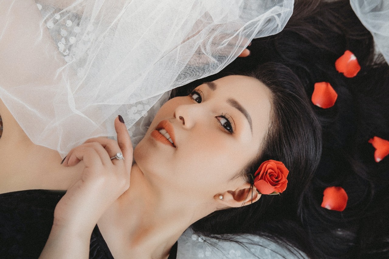 A woman laying down with her veil with roses and petals in her hair.